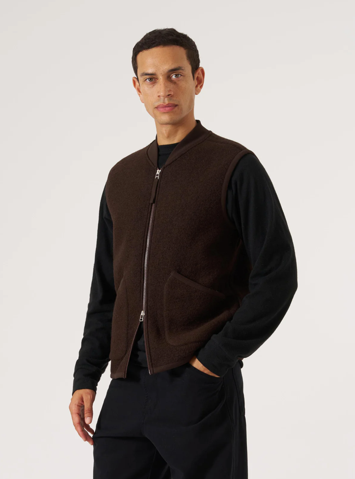 Man wearing a brown fleece vest over a black shirt on a white background.
