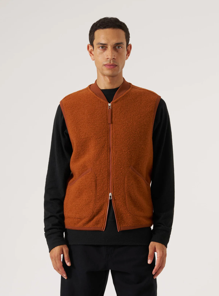 Man wearing an orange vest over a black shirt on a white background.