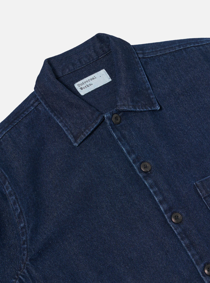 Close-up of a blue denim shirt with a collar and brand label on a light gray background.