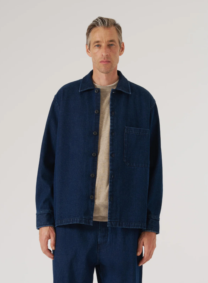 Man wearing a dark blue denim jacket over a beige shirt on a plain background.
